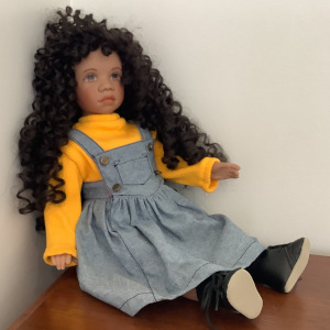 18-inch black Rudy doll in yellow sweater and denim jumper dress, with long curly black hair