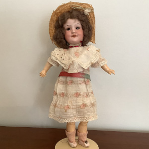 Antique Armand Marseille doll with short, curly brown hair and pink batiste print dress and lace trim with a straw hat