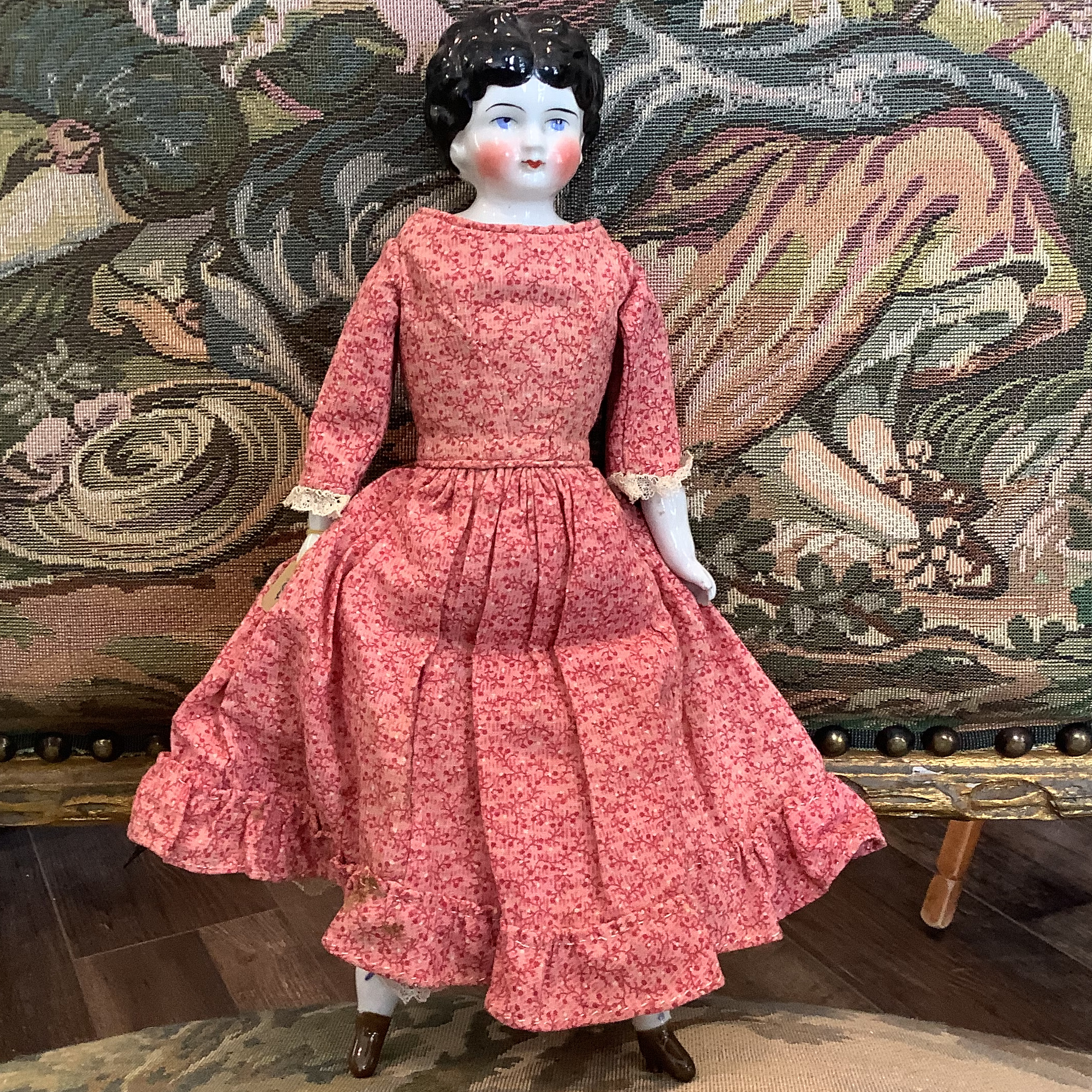 China doll with molded black hair and white skin in pink and red calico dress with tiny flowers