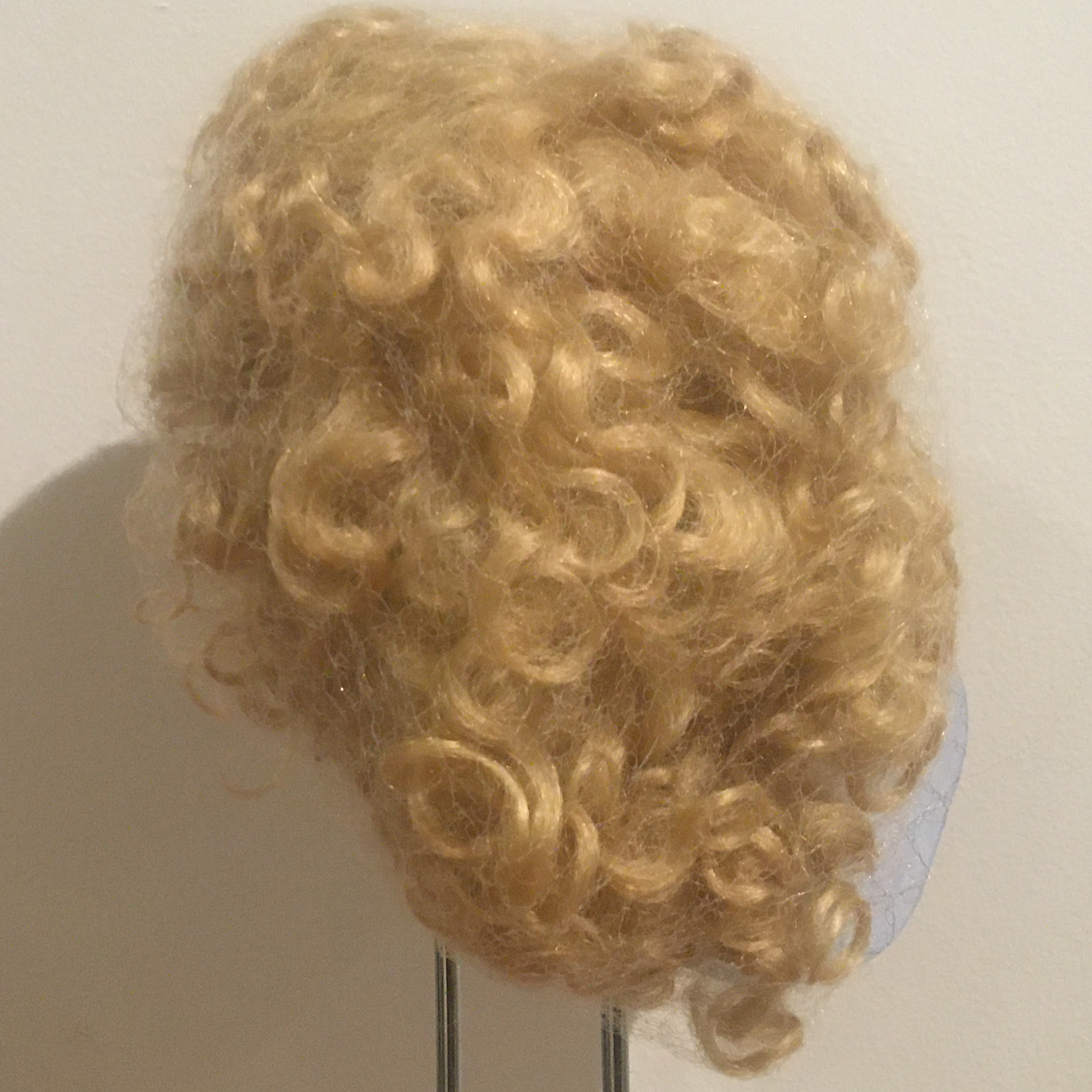 Light blond wig with allover curls, medium length, contained in a hair net