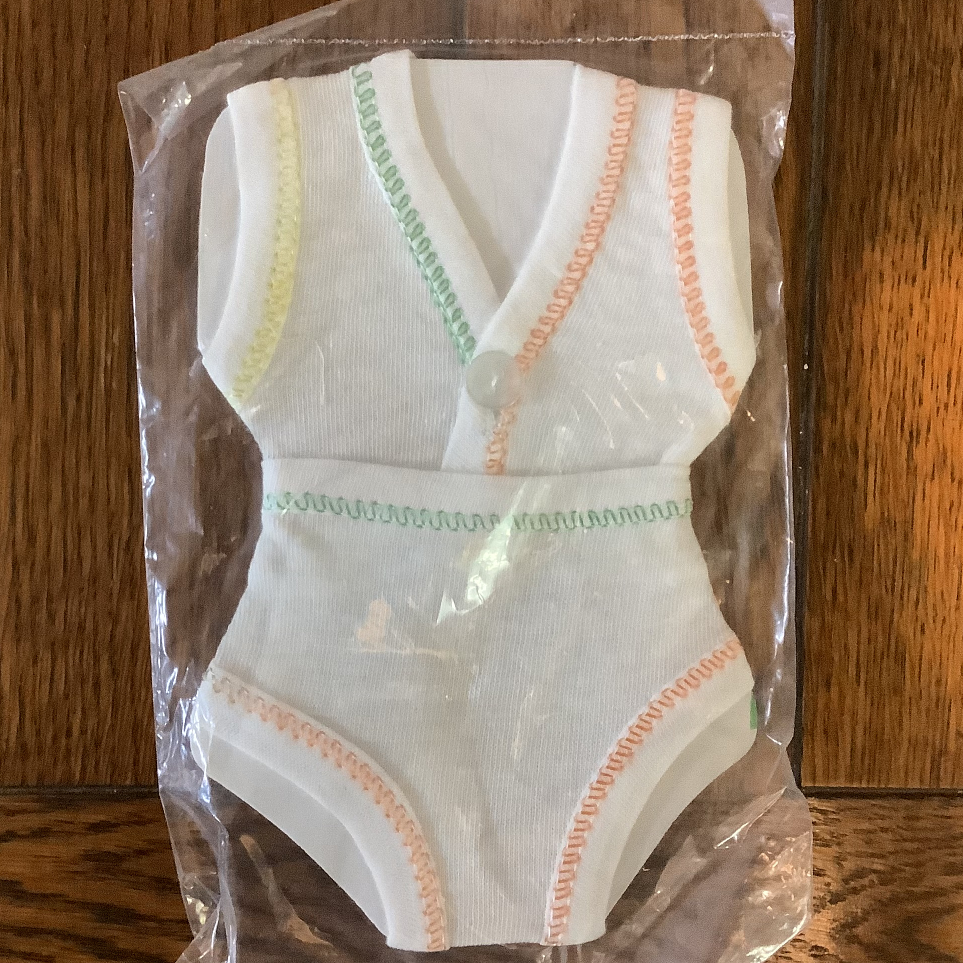 A set of white top and bottom underwear, edged in deliberately asymmetrical pattern of yellow, green and orange stitching, on a display card