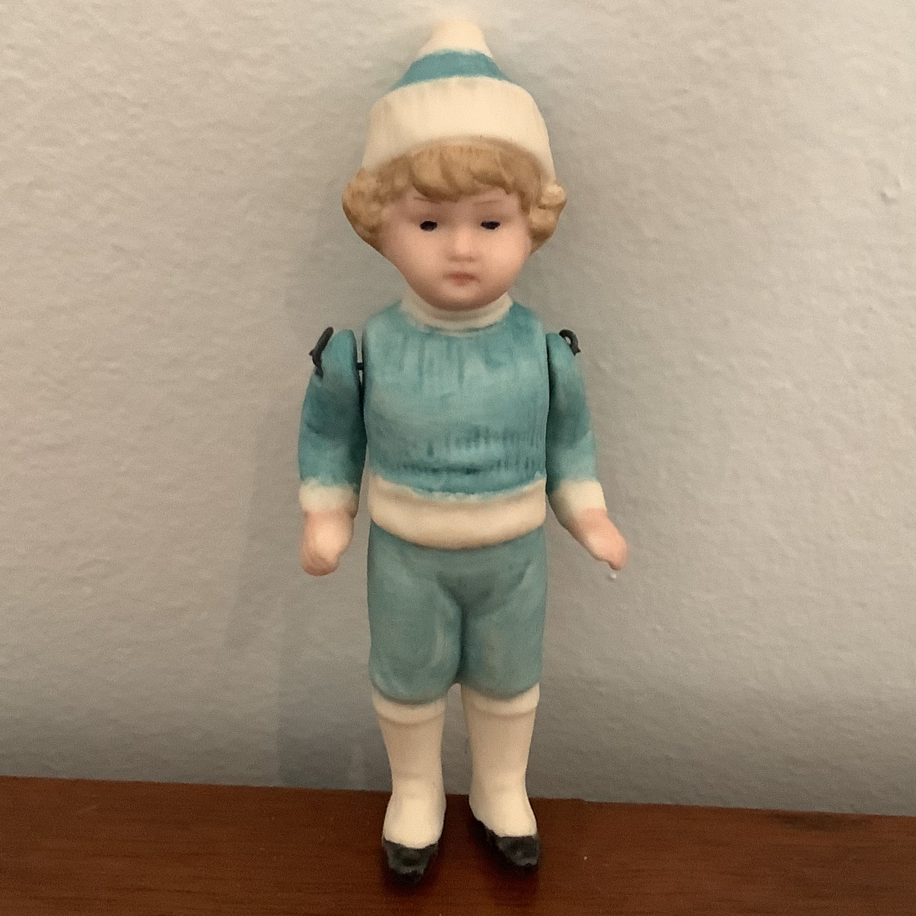 Small, blond, light-skinned doll with painted hair wearing blue painted sweater, hat and shorts