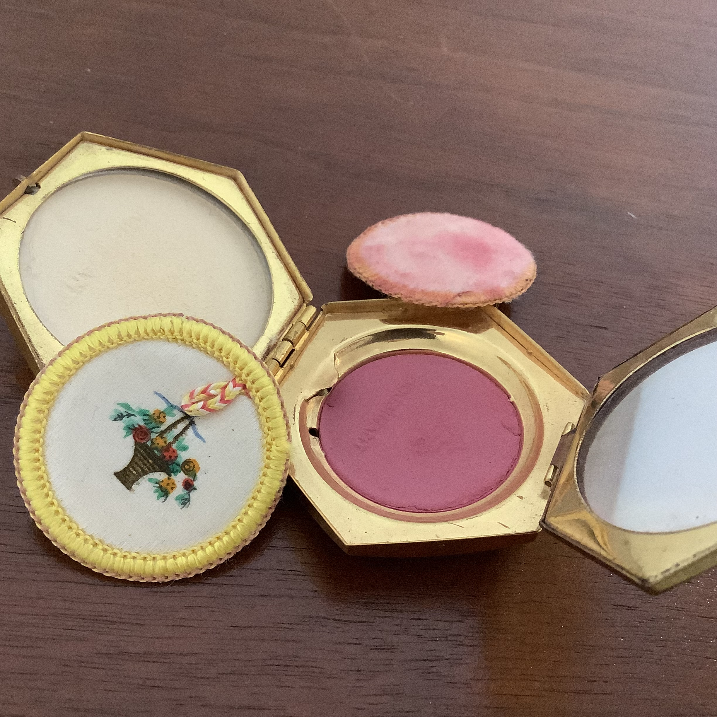 Open compact with powder puffs removed, revealing beige powder, pink blush and a mirror