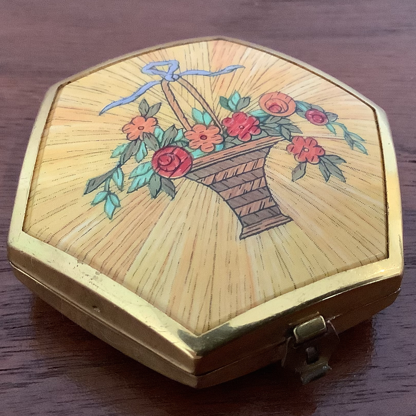 Closed compact with gold toned edges and a basket of flowers painted on the cover