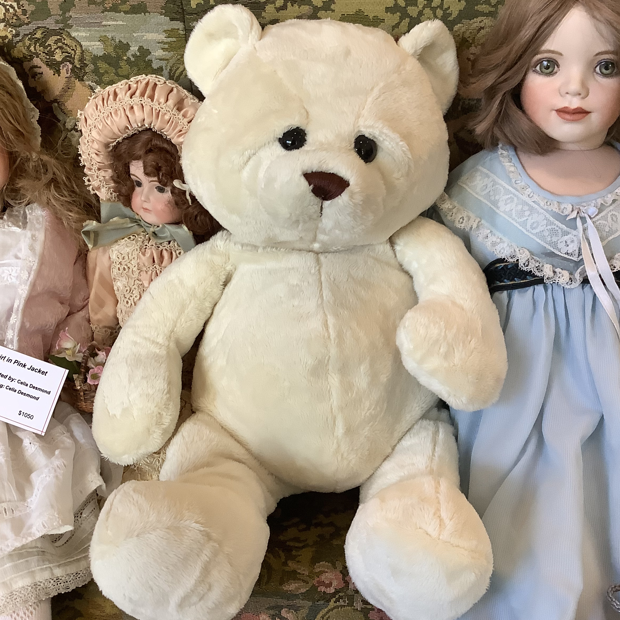 large white teddy bear sitting on couch with dolls