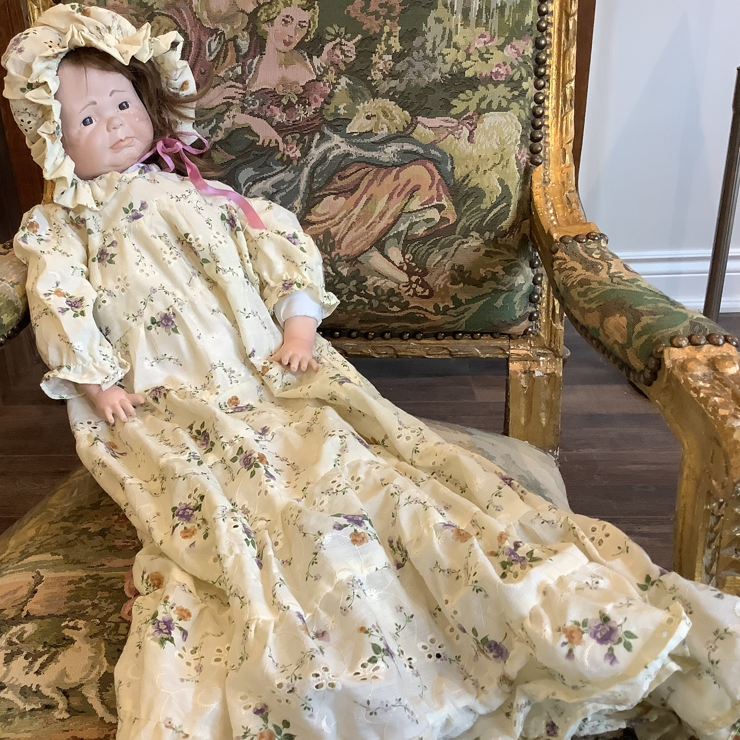 White baby doll in long yellow calico dress half-seated and half-lying in a chair