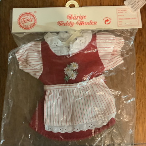 red corduroy dress in a package labelled in German, with white, red-striped cotton sleeves and white eyelet edges