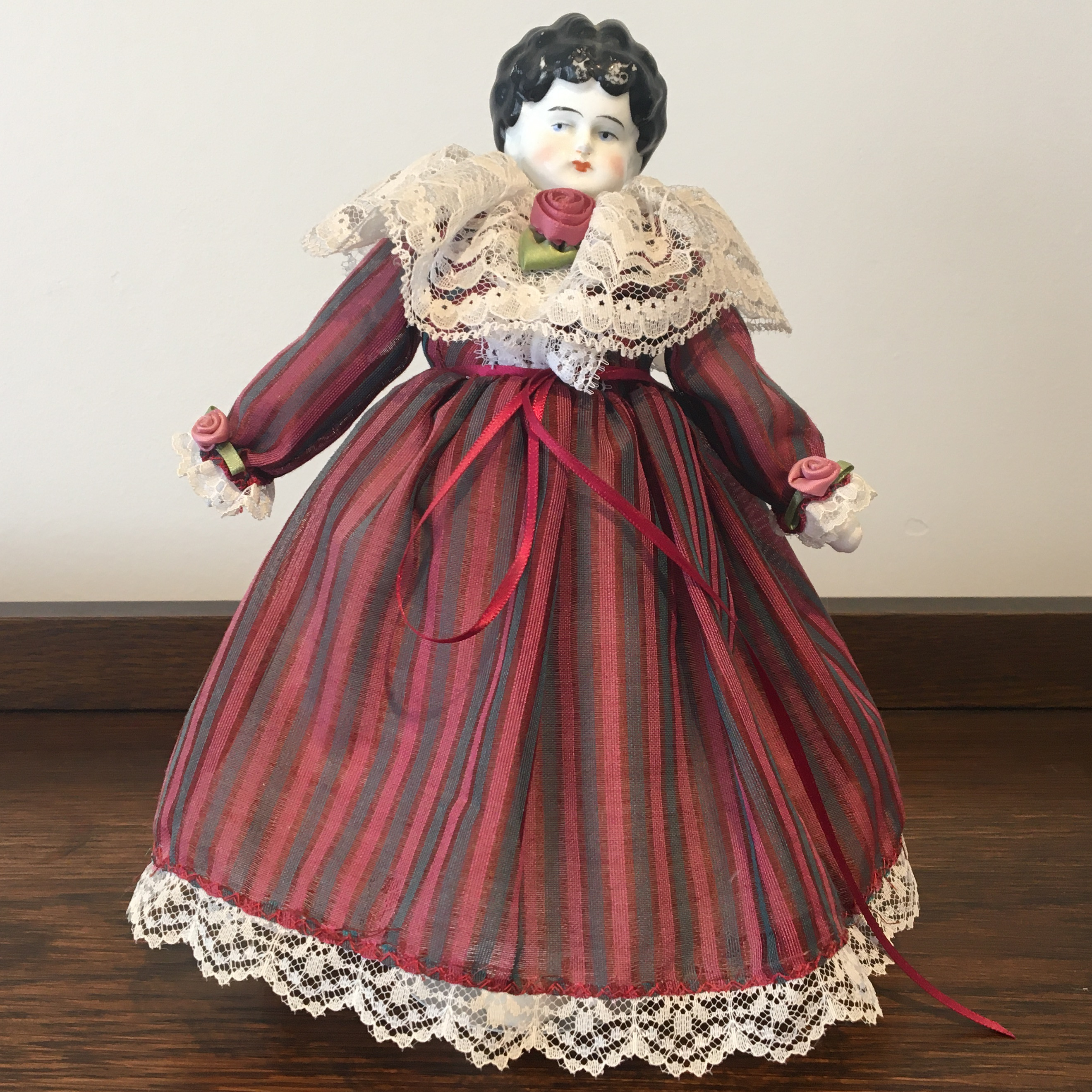 Antique china doll in a modern red and purple dress with vertical stripes and lace trim