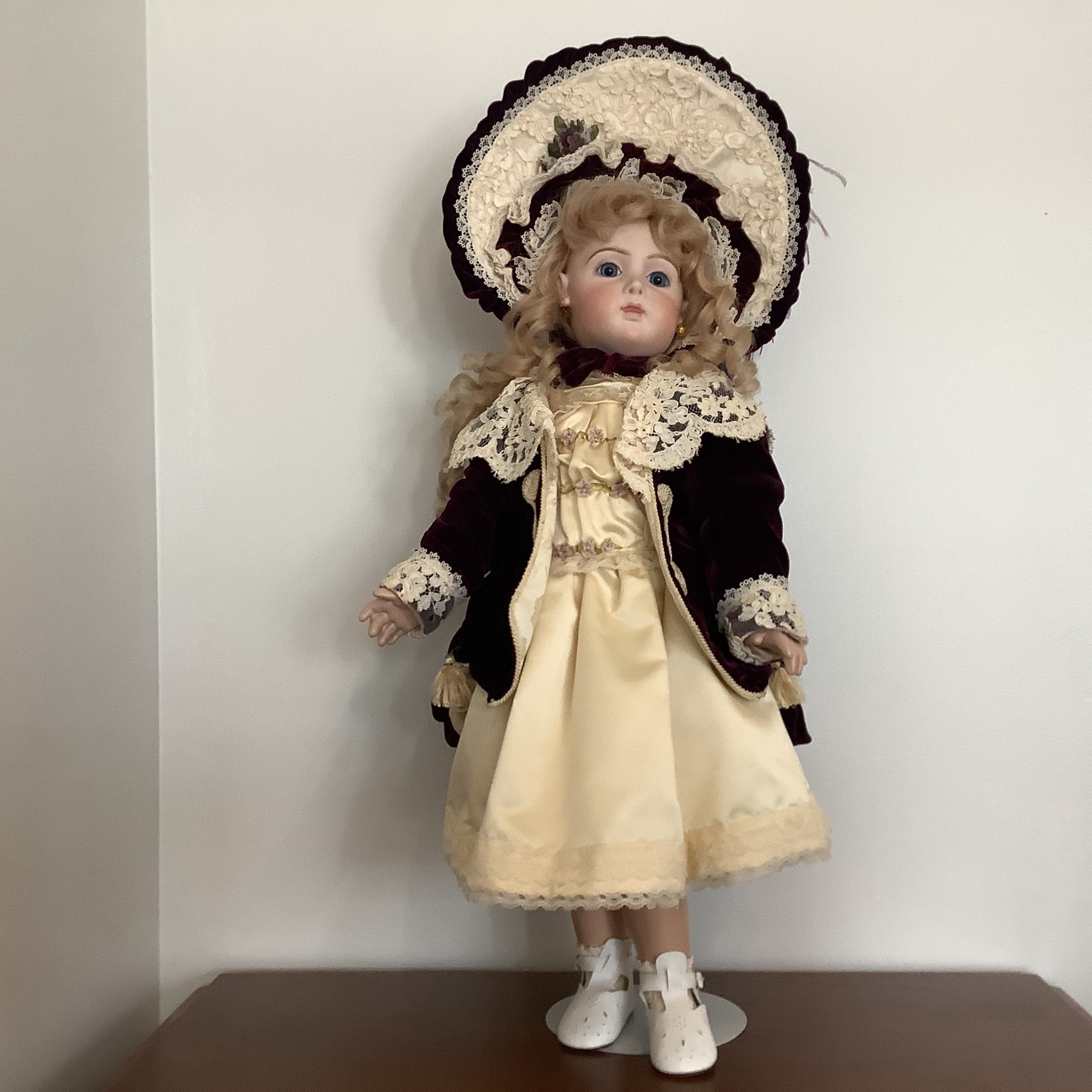 Reproduction Cody Jumeau doll in an off-white satin dress and lace-trimmed purple velvet coat and matching hat, with light skin and long, curly blond hair
