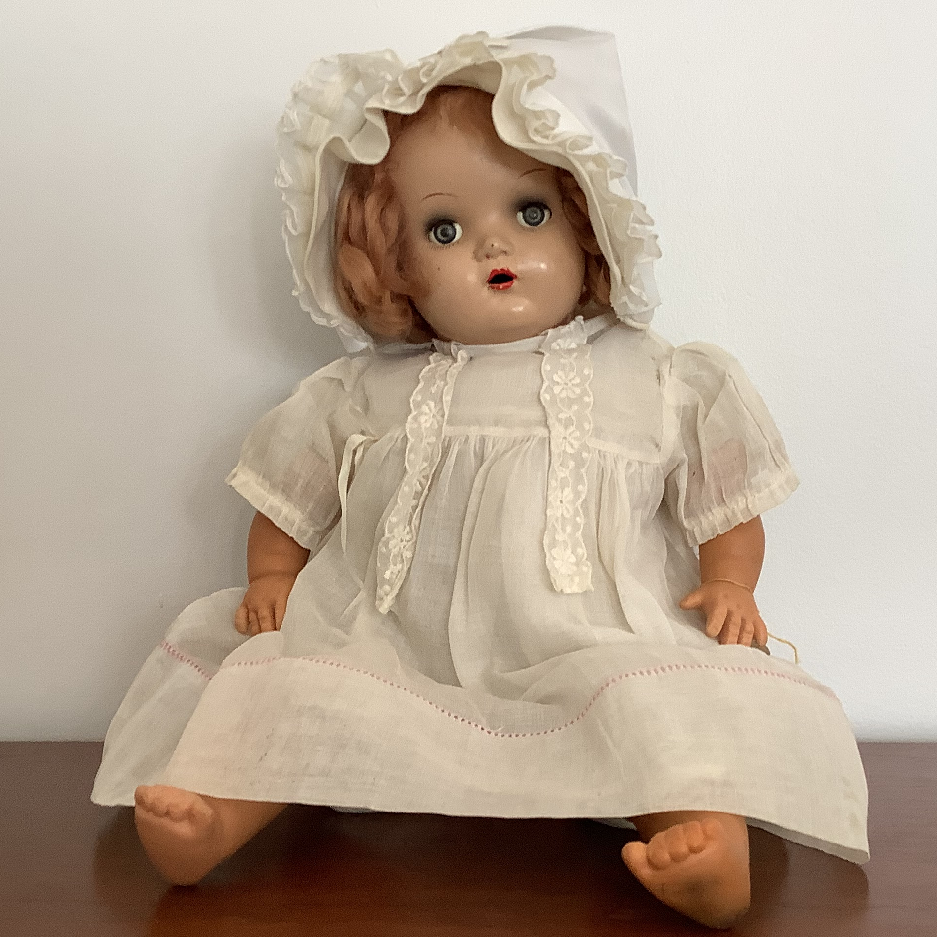Strawberry blonde vintage baby doll in sheer white cotton bonnet and dress, with sleep eyes and significant eye makeup