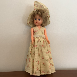 Small vinyl fashion doll with short blond hair, sleep eyes and printed calico dress and hat