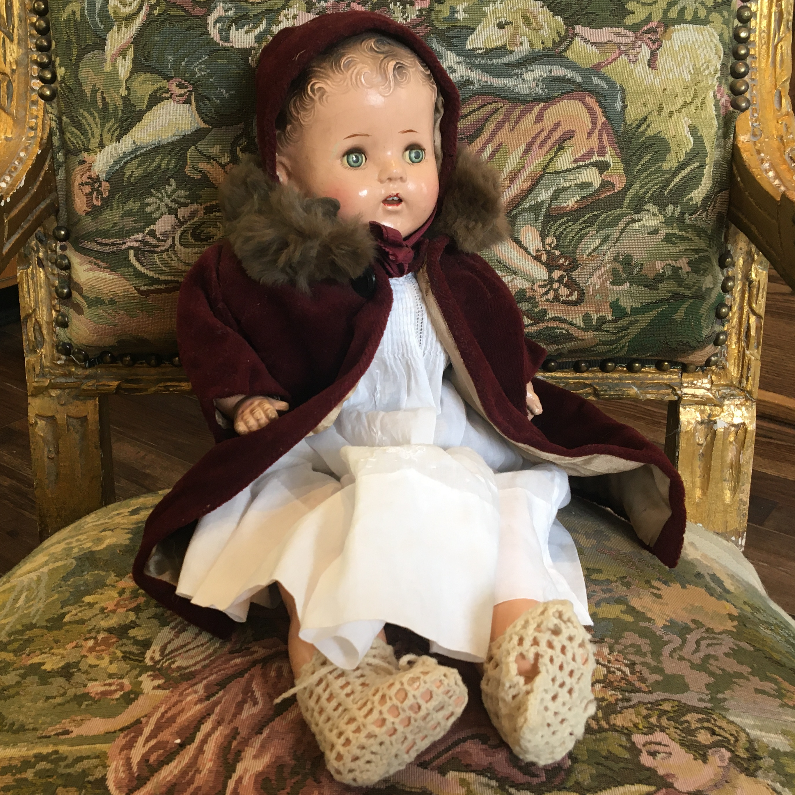 Light-skinned vintage baby doll in white cotton dress and burgundy corduroy coat and bonnet, with sleep eyes and dark molded hair