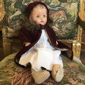 Light-skinned vintage baby doll in white cotton dress and burgundy corduroy coat and bonnet, with sleep eyes and dark molded hair