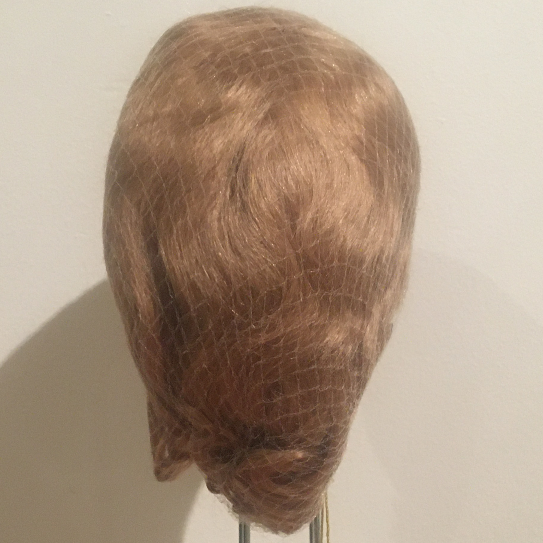 Reddish-blond or light red medium-length wig with short bangs, straight with slight wave, contained in a hair net