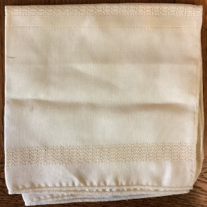 Square of off-white fabric with strips of fancy weaving along two edges