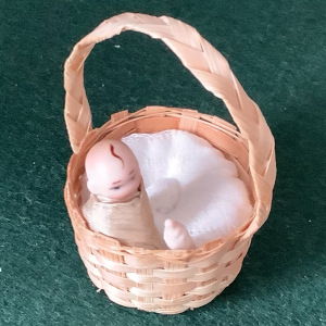 Very small baby doll in a miniature basket, about one inch long