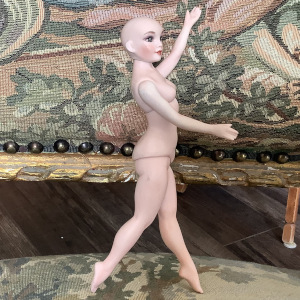 Nude female doll in dancing pose with bald head and body stringing protruding from crown of head