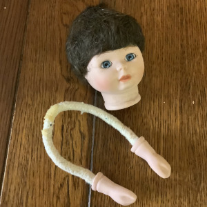 Small painted light-skinned doll head with short, dark-brown hair and blue eyes, and a pair of matching doll hands