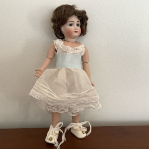 Small, light-skinned doll with short, wavy dark brown hair and white slip and shoes