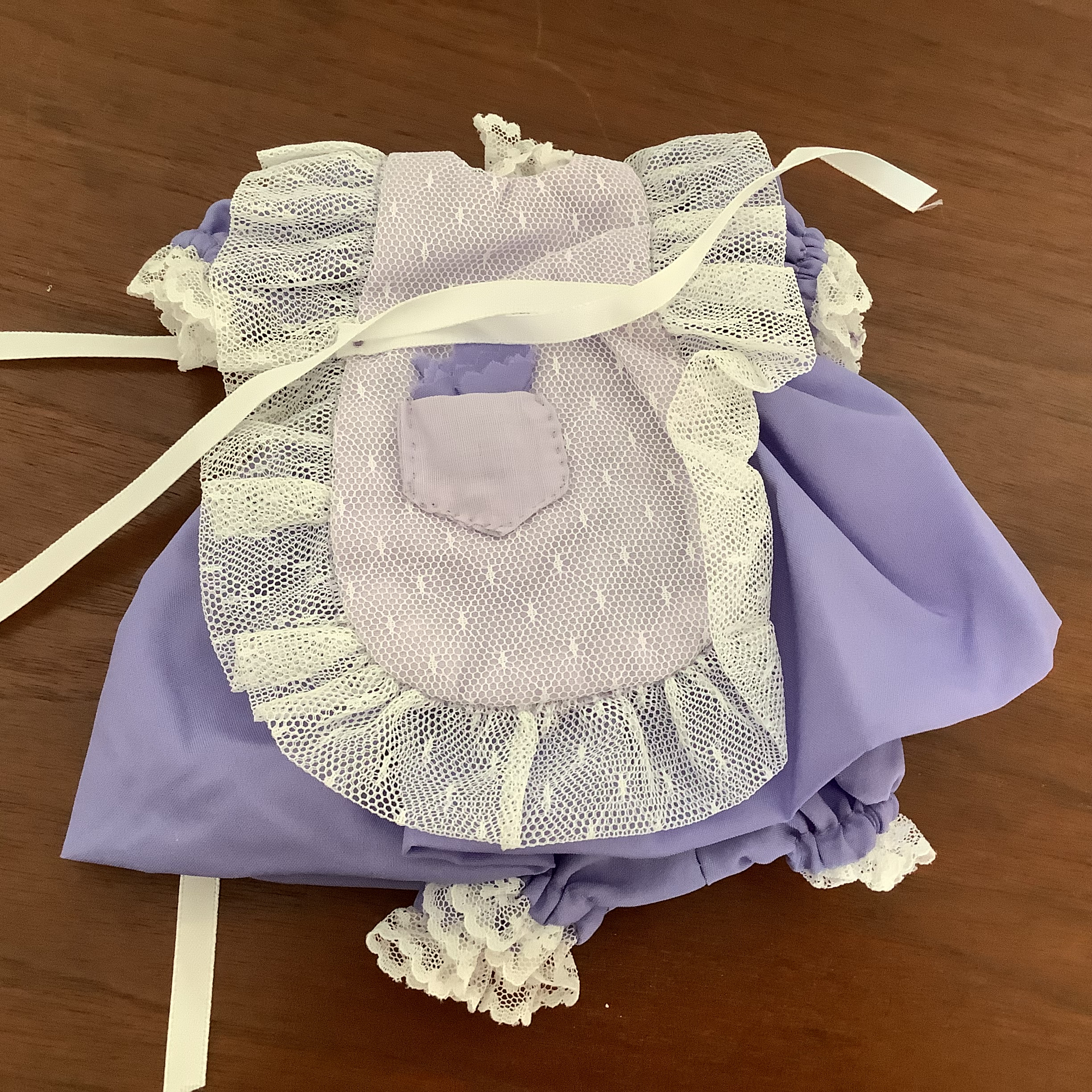 Purple dress with gathered skirt and matching bloomers, partially obscured by a white apron with lace edges