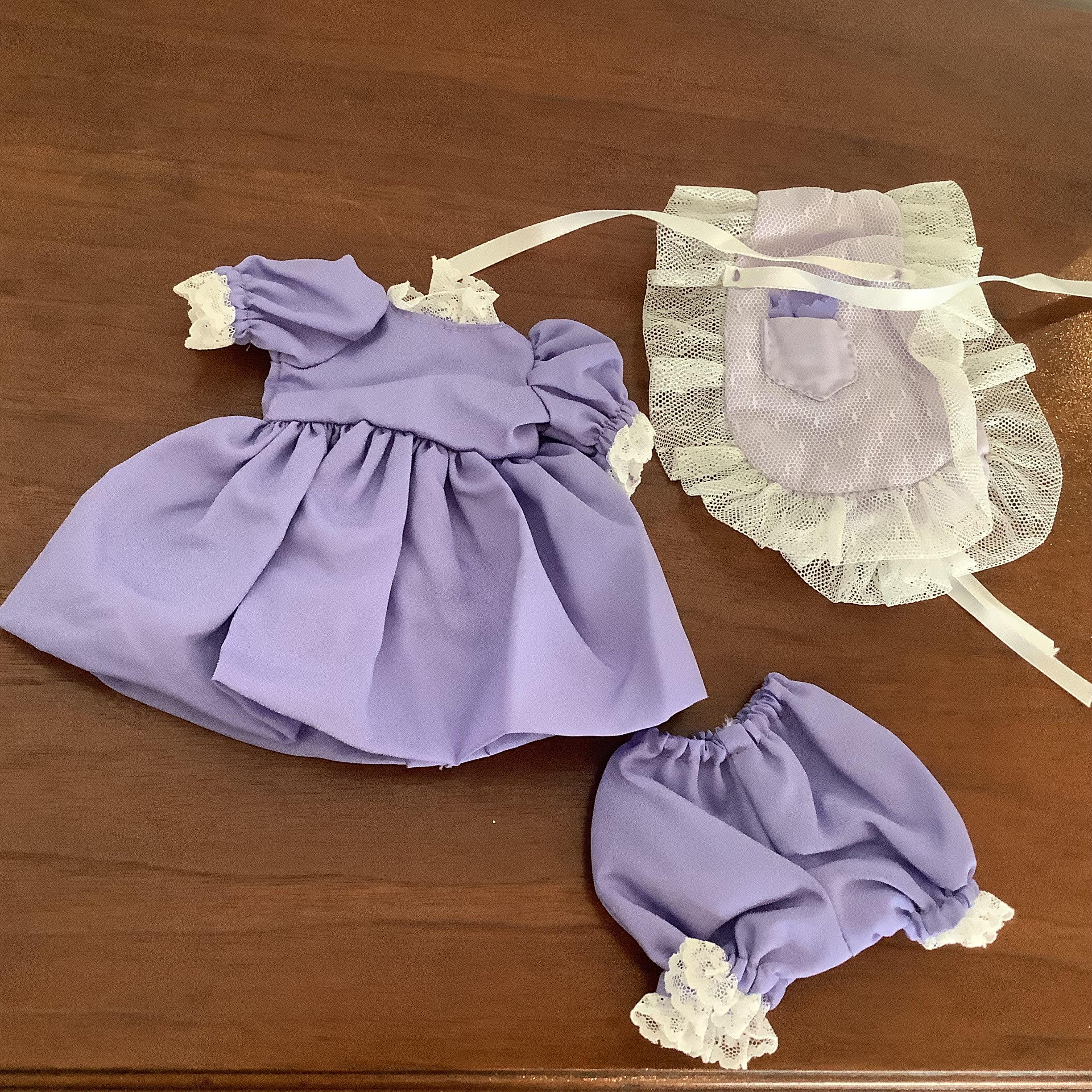 Purple dress, purple bloomers and white apron lying apart