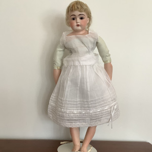 Antique doll, light-skinned with short blond hair, in a cotton slip dress, with some wig deterioration