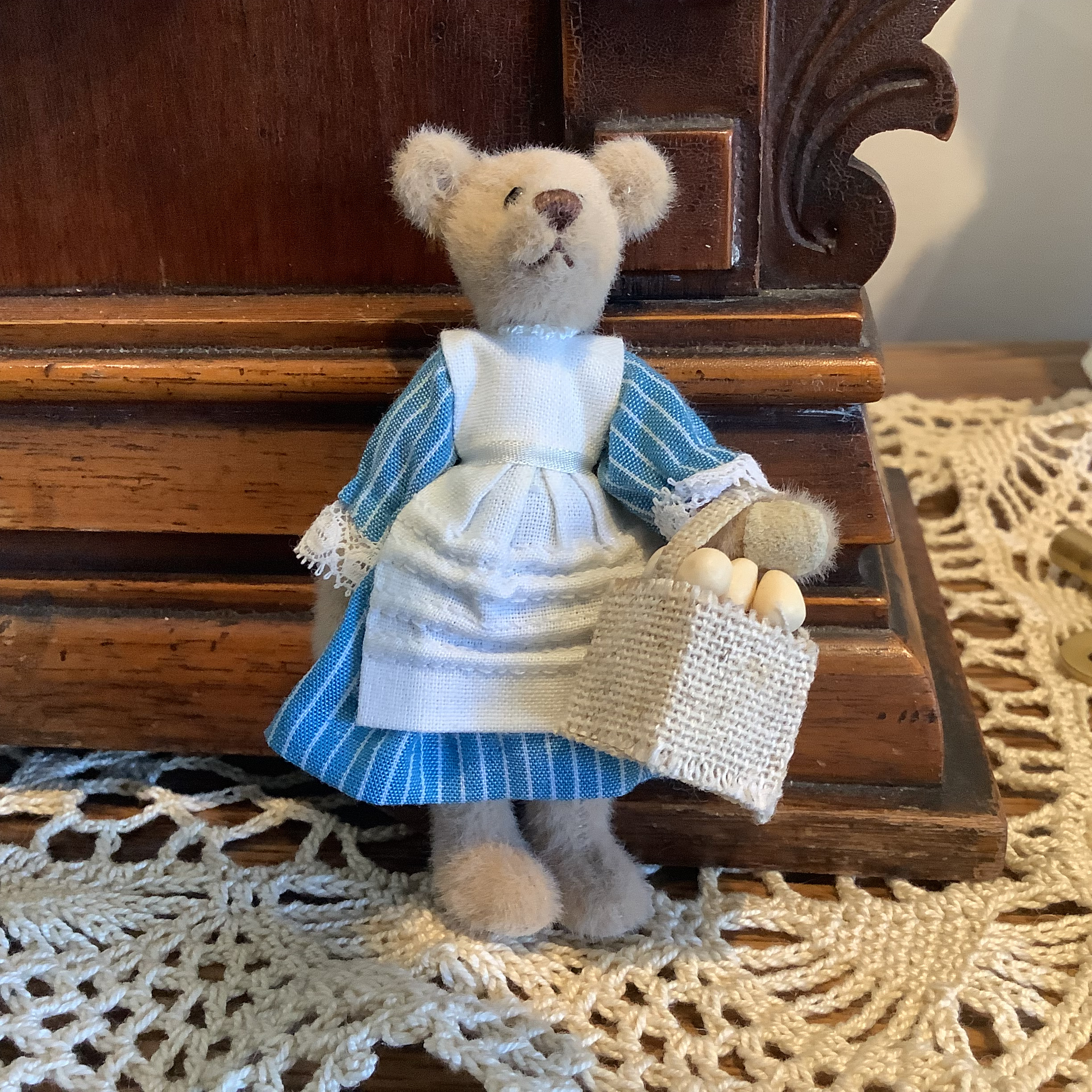 Small teddy bear doll in blue dress carrying a basket of eggs