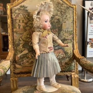 Medium-sized, light-skinned doll with curly blond hair and light coloured suit with lace trim