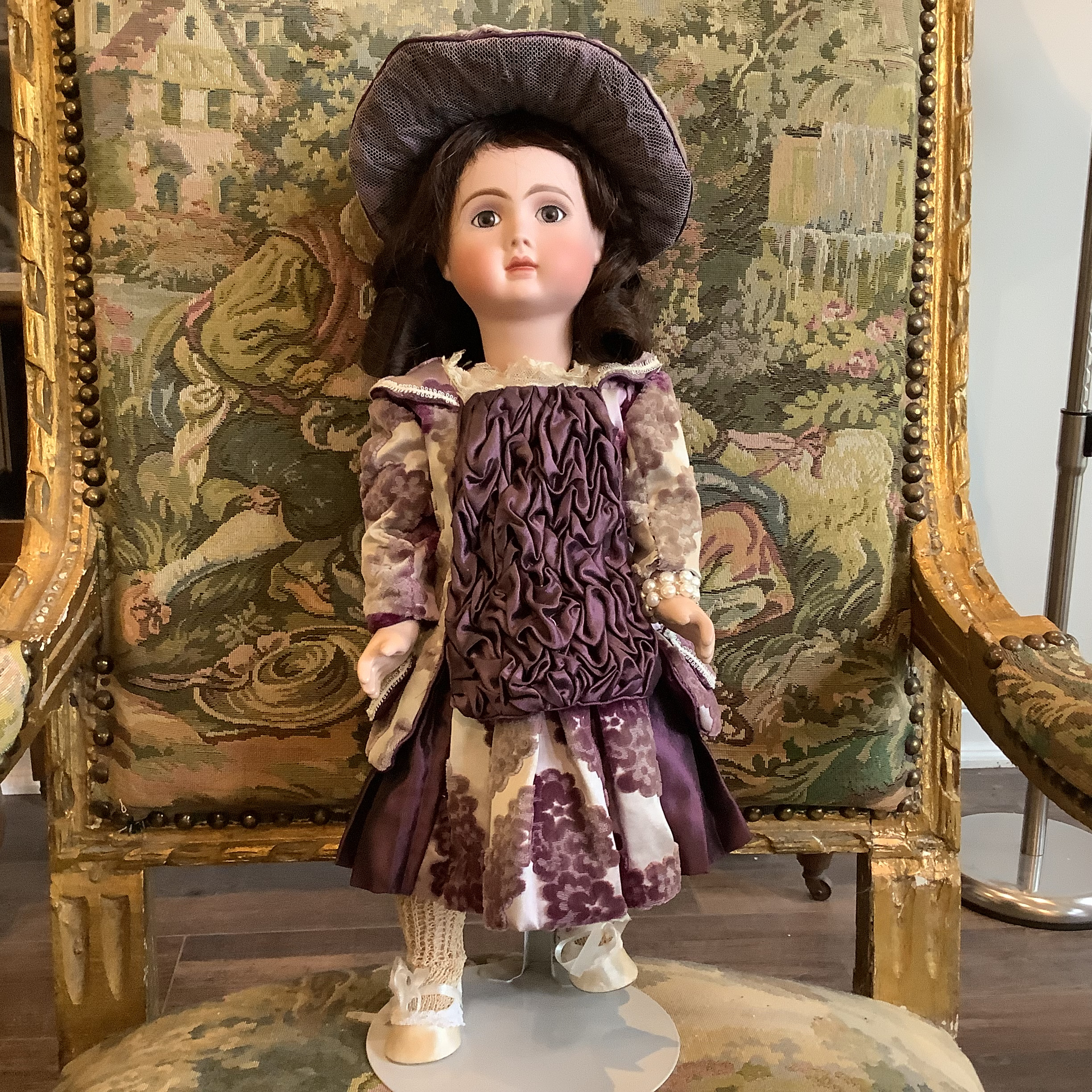 Doll with long, straight brown hair wearing a dress and matching hat in purple and beige