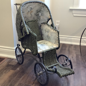 Dark grey-green wicker baby carriage with grey-on-white interior upholstery and metal wheels