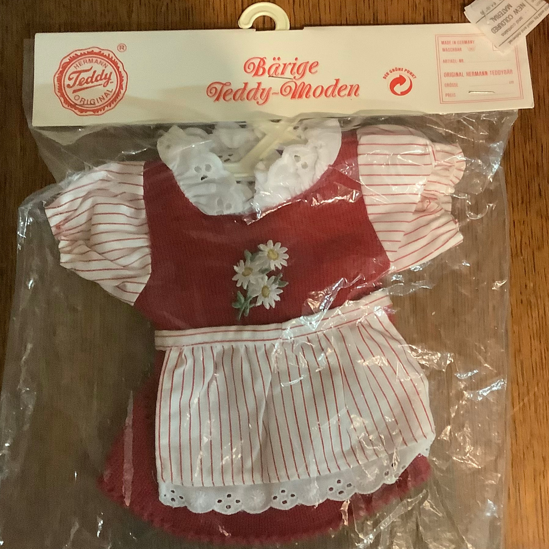 red corduroy dress in a package labelled in German, with white, red-striped cotton sleeves and white eyelet edges