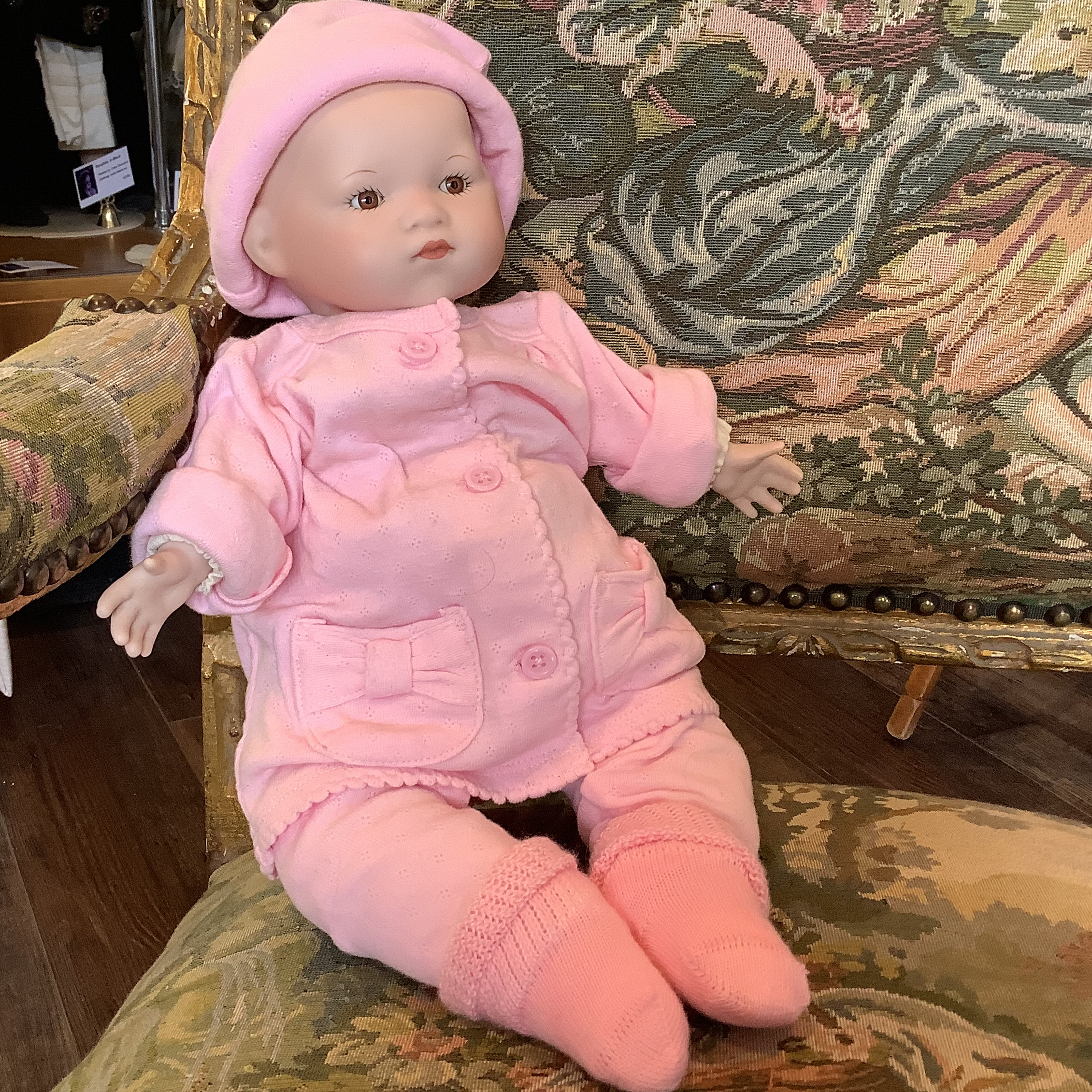 Reproduction Baby Bye-Lo doll in modern pink onesie with matching hat, seated on a chair